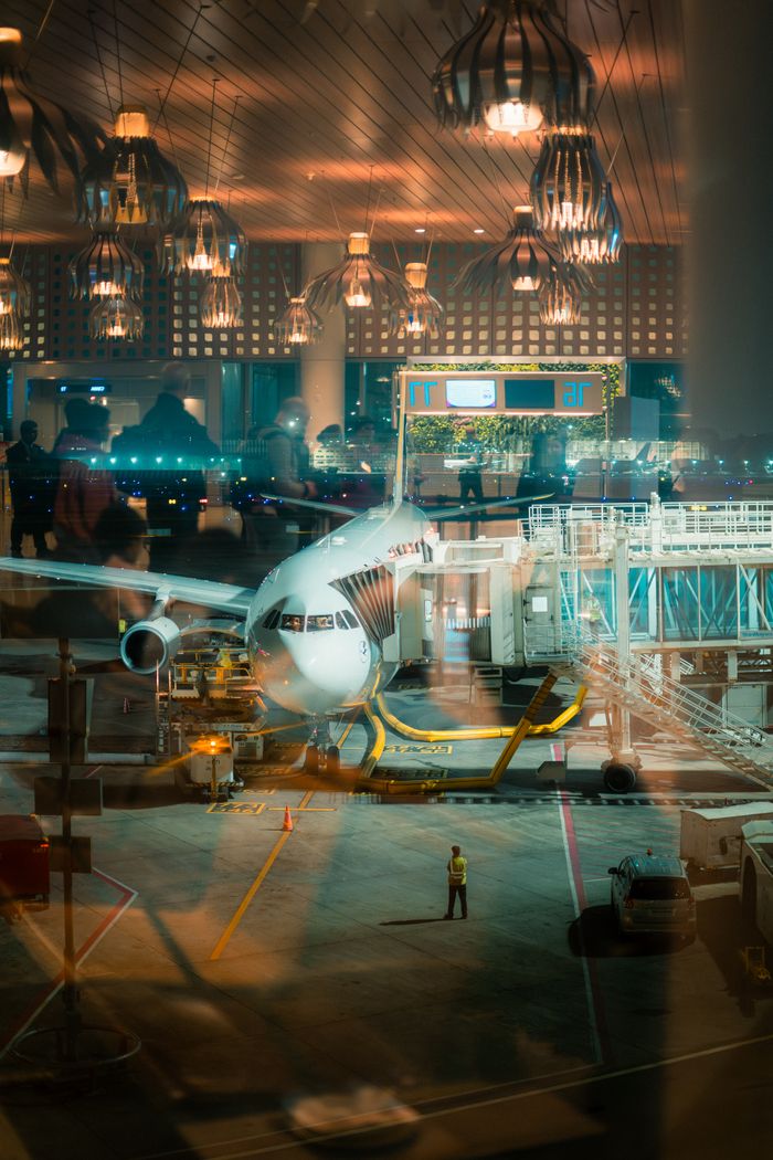 A parked airplane at Mumbai Airport gate with reflections, captured during the night.